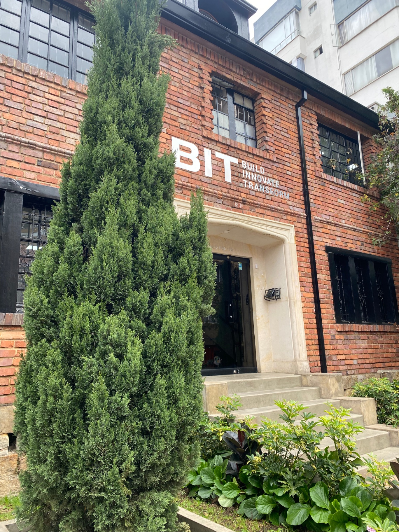 Fachada de la sede de BIT en Bogotá: edificio de ladrillo con el letrero BIT — Build Innovate Transform sobre la entrada principal